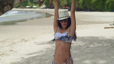 On-the-white-sands-of-a-tropical-Caribbean-beach,-a-girl-in-a-bikini-relishes-the-sun-while-swinging-from-a-tree-branch