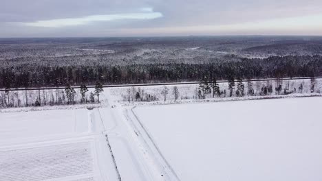 Aerial-view-over-snow-covered-field-and-road-with-parked-car-near-massive-forest
