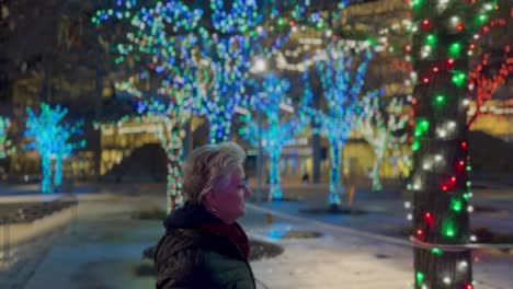 Senior-woman-walking-in-a-city-at-night-decorated-with-Christmas-lights