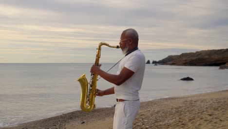 Weitwinkelaufnahme-Eines-älteren-Afrikanischen-Mannes,-Der-Während-Der-Goldenen-Stunde-Am-Strand-Saxophon-Spielt