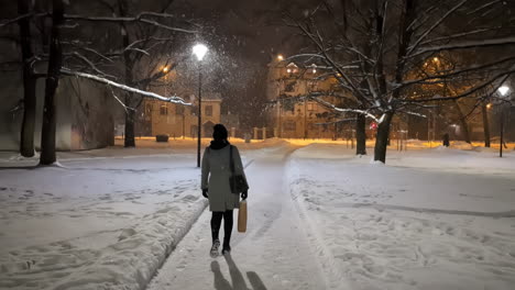 Woman-walking-through-a-city-park-at-night-as-it-snows---slow-motion