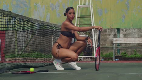 On-a-sunny-day,-a-girl-in-a-thong-bikini-plays-tennis-with-enthusiasm-on-the-court-while-squating