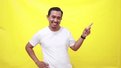 Happy-asian-man-making-choice,-pointing-fingers-and-showing-sideways,-smiling-at-camera,-standing-over-yellow-background