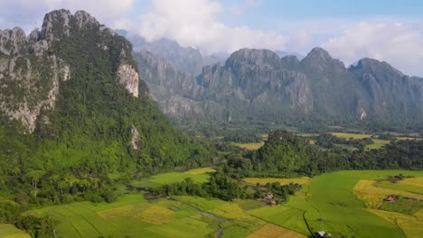 Aerial-View-Of-Green-Farming-Fields-With-Soaring-Forested-Mountain-Landscape-At-Vang-Vieng
