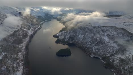 Lake-in-winter-countryside-landscape-with-flight-just-below-low-cloud-level-towards-bright-cloudy-valley-end