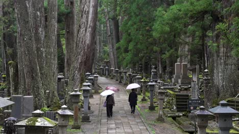 Group-Of-Visitors-Holding-Umbrellas-Walking-Along-Path-At-Okunoin-Cemetery-In-Koya-San
