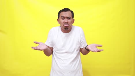 Asian-man-shrugs-shoulders-unaware-raises-hand-clueless-has-no-idea-cannot-answer-poses-against-yellow-background