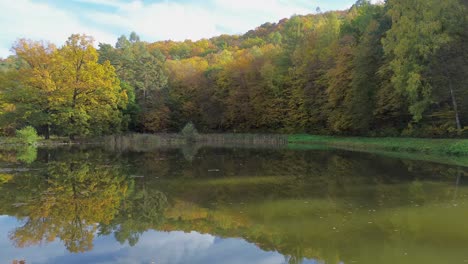 Ein-Blick-Auf-Den-Bunten-Wald,-Der-Alle-Farben-Des-Herbstes-Aufweist,-Von-Der-Oberfläche-Des-Teiches-Aus