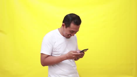 Asiatischer-Erwachsener-Mann-Hält-Mobiltelefon-In-Der-Hand,-Nutzt-Virtuelle-App,-Online-Dienst-Auf-Dem-Smartphone,-Schreibt-SMS,-Chattet,-Tippt-Nachrichten,-Berührt-Den-Bildschirm,-Steht-Isoliert-Auf-Gelbem-Hintergrund
