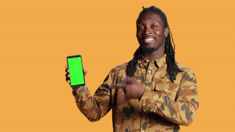 Smiling-man-points-to-smartphone-with-greenscreen-on-camera