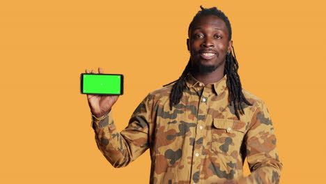 Cheerful-adult-holds-smartphone-with-greenscreen-in-studio