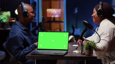 Green-screen-laptop-next-to-man-on-podcast-discussing-with-guest-during-marathon-stream