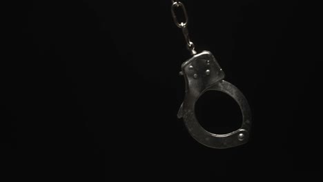 Close-up-of-Handcuff-Swinging-in-Black-Background