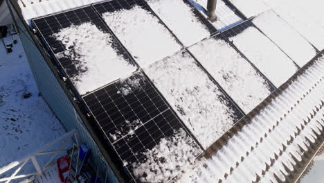 Drone-shot-around-partly,-wet-snow-covered-solar-cells-on-a-house-roof,-winter-day