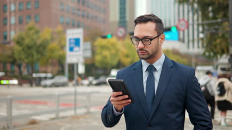 Businessman-Manager-reading-email-on-phone-in-large-city-downtown-area-with-traffic-in-background