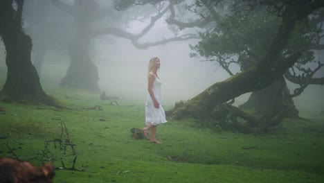 Attractive-blond-woman-in-angelic-dress-walks-in-eerie-enchanted-foggy-forest
