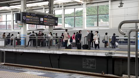Commuters-Waiting-On-Platform-At-Hiroshima-Station-With-Bullet-Train-Departing-In-Background