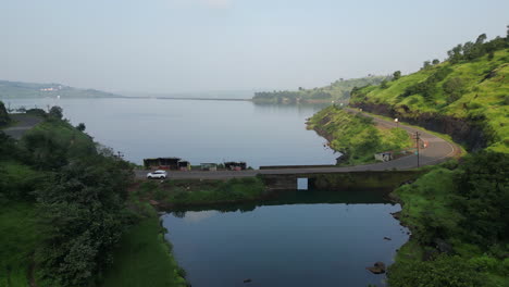 Aerial-top-view-of-road-through-green-woods-and-blue-lake-Nashik-Maharashtra-4K-Drone