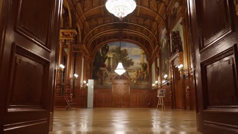 Going-into-wooden-ballroom-with-paintings-and-chandeliers-hang-from-ceiling
