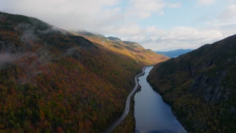 Aerial-view-of-a-lake-surrounded-with-fall-foliage-as-cars-passing-by-on-the-road-in-Upstate-New-York