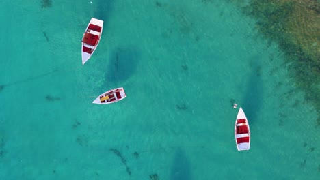 Drone-orbit-and-rises-as-small-white-rowboats-anchored-in-clear-blue-water-cast-shadow-on-sand