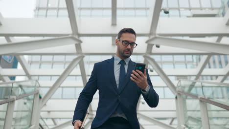 Businessman-rushes-down-staircase-holding-notebook-reads-message-on-phone-on-the-go