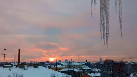 Wunderschöner-Sonnenuntergang-über-Einer-Verschneiten-Stadt-Mit-Eiszapfen-Im-Vordergrund