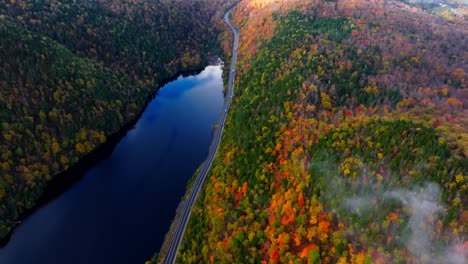 Early-morning-aerial-footage-of-a-lake-surrounded-with-fall-colors-in-Upstate-New-York-showing-a-road-as-cars-passing-by