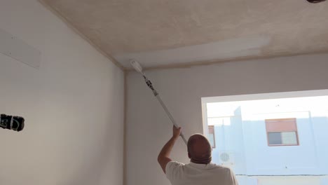 Person-is-using-painting-roller-and-adding-paint-to-wall-top-ceiling-surface,-tradesman-responsible-for-the-painting-and-decorating-of-buildings
