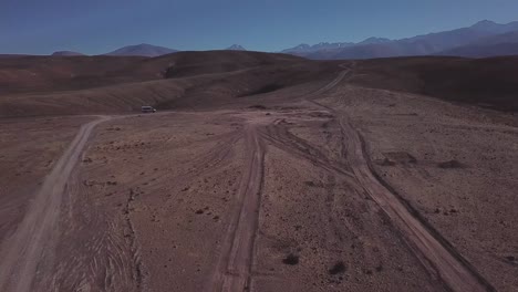 Car-driving-on-a-dusty-road-in-the-Atacama-Desert-with-an-arid-landscape-in-Northern-Chile,-South-America