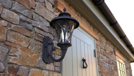 Close-up-movement-of-old-fashioned-gas-lamp-on-the-outside-of-a-luxury-rustic-stone-walled-building-next-to-the-front-door-in-the-shadows
