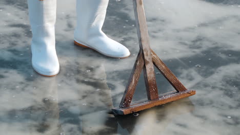 Person-In-White-Boots-Standing-At-A-Salt-Flat-With-a-Wooden-Rake-At-Gaetgol-Eco-Park-In-South-Korea