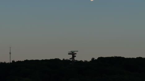 Moon-disappearing-from-view,-Wilhemina-tower-under-fading-sunset