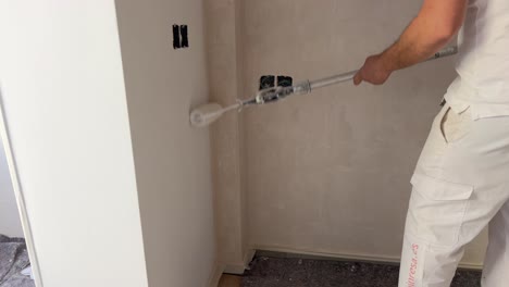 Person-is-using-white-color-painting-roller-and-adding-paint-to-wall-surface