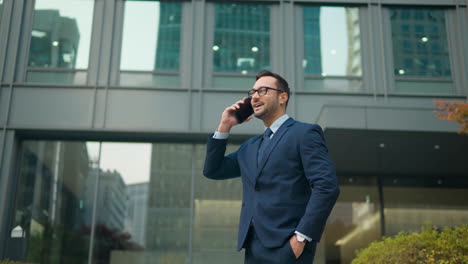 Businessman-talking-on-phone-standing-outside-building,-hand-in-suit-pocket,-
