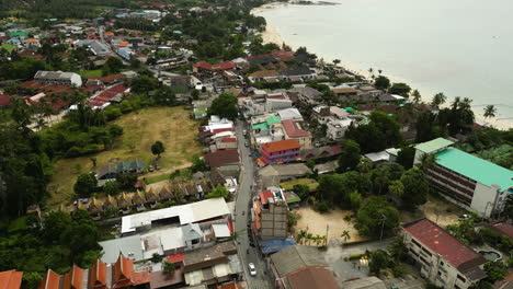 Aerial-flyover-tourist-town-in-koh-tao-Thailand-with-traffic-on-main-road-during-cloudy-day