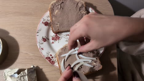Adding-fresh-onion-on-top-of-liver-pate-sandwich,-top-down-view