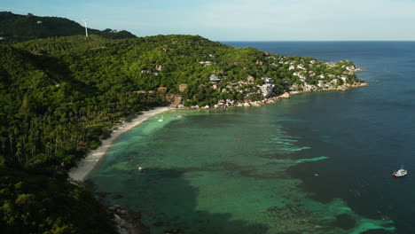 Aerial-view-of-sandy-beach-with-clear-bay-water-in-front-of-green-hills-on-Koh-Tao-at-golden-sunset