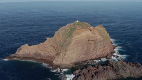 Gran-Roca-En-Un-Sereno-Océano-Turquesa-Con-Un-Pequeño-Faro-En-La-Parte-Superior