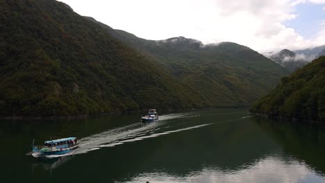 Serenity-on-the-Alpine-Waters:-Boats-Sailing-Amidst-the-Calm-Beauty-of-Koman-Mountain-Lake-in-Albania,-Cloudy-Day-Valley