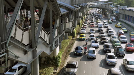 People-seen-using-the-elevated-walkway-from-one-station-to-another-then-to-train-platforms-while-the-road-on-the-right-is-already-congested-and-yet-flowing,-Bangkok,-Thailand
