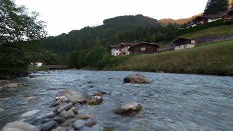 Idyllic-flowing-river-next-to-a-group-of-holidays-houses-in-a-mountain-range-from-a-low-perspective