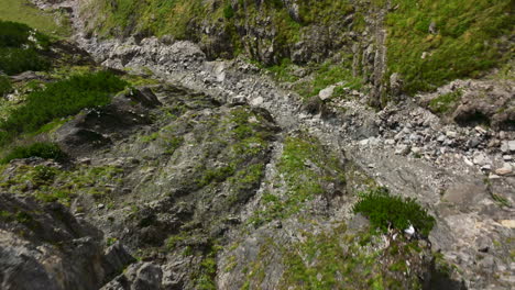 Descending-drone-shot-of-rocky-dried-up-river-running-from-mountaintop-in-midst-of-Austrian-Alps-mountain-range