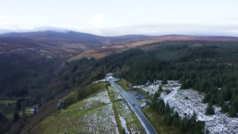 Aerial-View-of-a-Car-Driving-Through-Snow-Covered-Forest-In-The-Wicklow-Mountains,-With-People-Enjoying-The-Snowy-Forest-Backdrop