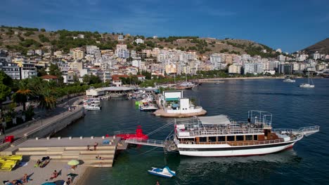 Tranquil-Pier-Along-Saranda's-Coastal-City,-Boats-and-Tour-Ships-Anchored-in-the-Blue-Bay-for-Summer-Leisure