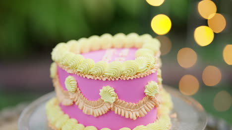Pink-And-Yellow-Heart-Shaped-Cake,-Close-Up-Slow-Motion-With-Fairy-Light-Background-4K