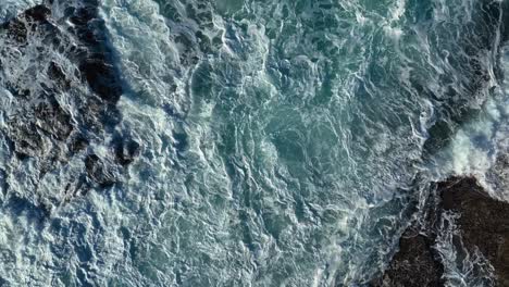 Top-View-Of-Strong-Waves-Crashing-At-Rocky-Sea-Cliffs-With-Breaking-White-Foam