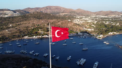 Türkische-Flagge-Mit-Blick-Auf-Das-Meer-Und-Die-Berglandschaft-In-Gümusluk,-Bodrum,-Türkei
