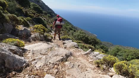 Man-with-backpack-walking-on-edge-of-cliff-of-high-rocky-mountain-on-Lycian-Way,-Turkey