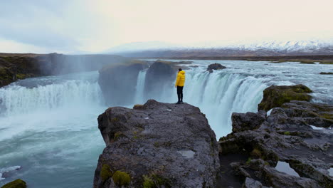 Man-On-The-Cliff-Next-To-Godafoss-Waterfall-In-Iceland---Drone-Shot